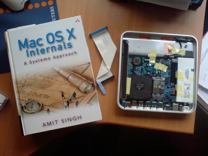 A book entitled Mac OS X Internals next to an opened up AppleTV showing its internal circuit boards.