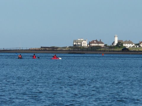 A photo of blue water and sky, which a thin strip of West Kirby buildings in between. In the water you can make out three red splodges that are us kayaking.