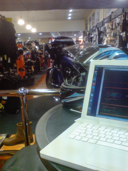 A view of a motorbike dealership from the inside, sat at a table, upon which is a motorbike helmet and an Apple iBook.