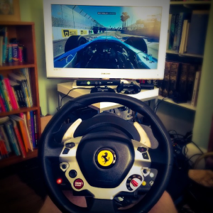 A view of a TV playing a car video game with in cockpit view, with a racing wheel in front of it.
