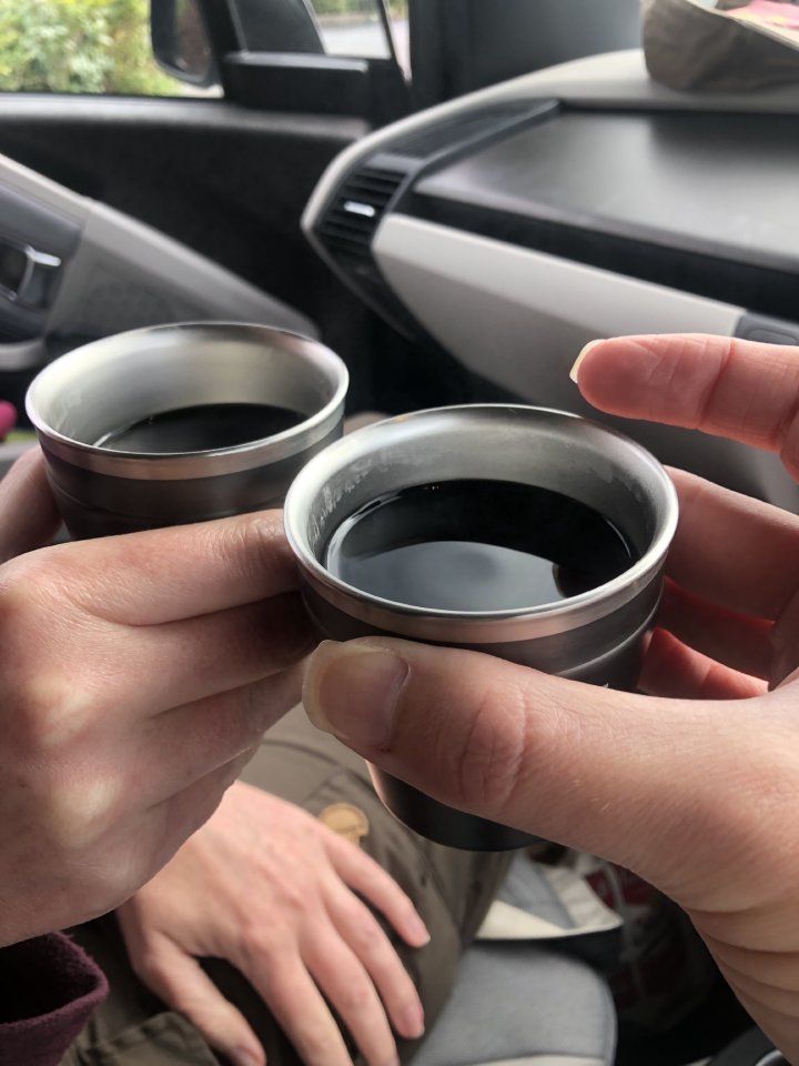 A photo of two cups of black coffee, held by me and Laura respectively, inside the car