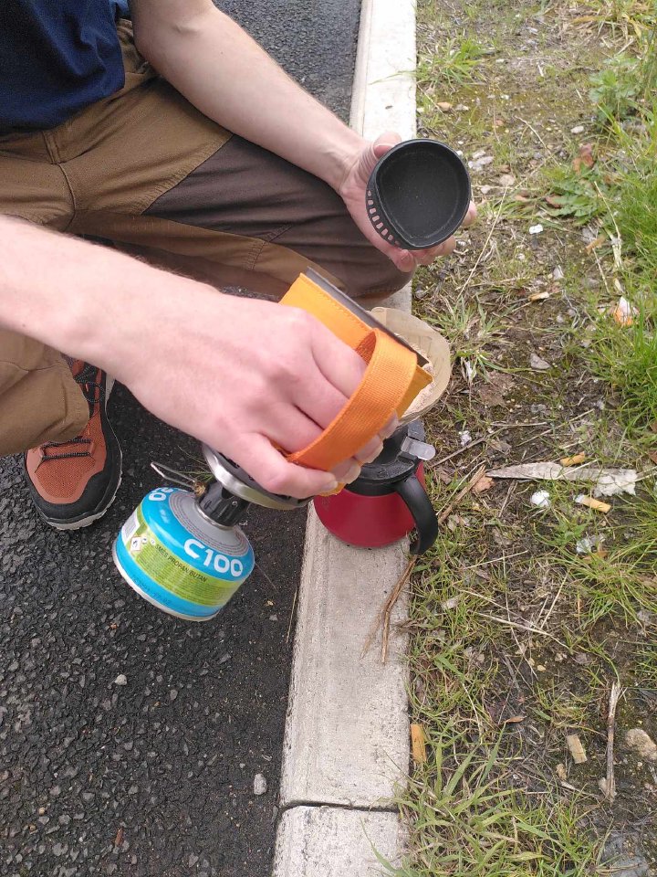 A shot of me crouched down next to the curb pouring water from the small primus boiler into the V60