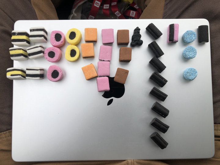 A photo of a MacBook Pro laptop sat on my lap, on which has been arrange a histogram of colourful sweeties, showing which ones are more popular (the plain licquorise).