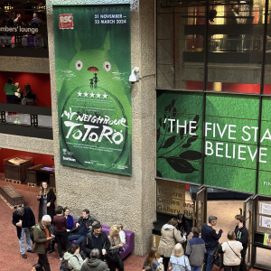 A photo of the inside of the Barbican theatre lobby showing a large hanging sign advertising My Neighbour Totoro.