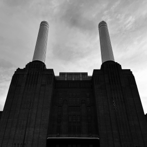 A black and white photo of the front of Battersea Power Station, showing a silhouette of the main brick building and two of the tall chimneys