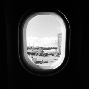 A photo out of the window of a plane, with the inside in shadow, and outside you can see an airport in the sun with another plane parked a bit away.