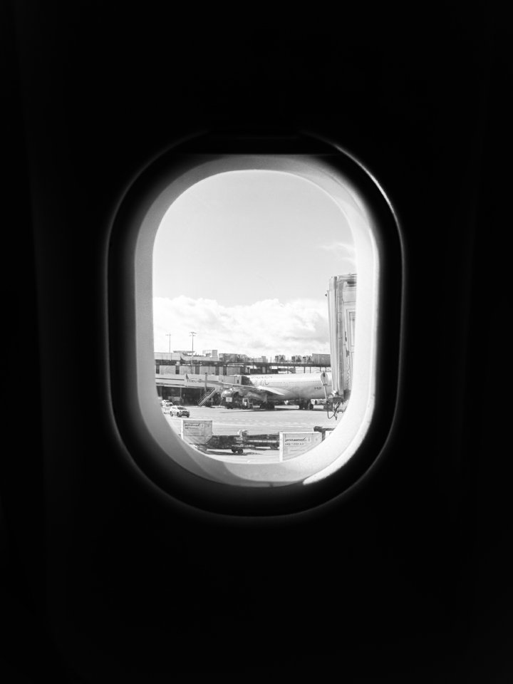 A photo out of the window of a plane, with the inside in shadow, and outside you can see an airport in the sun with another plane parked a bit away.