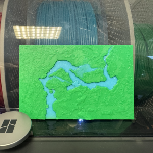 A photo of a small plastic 3D-print showing a blue river running through a green landscape.