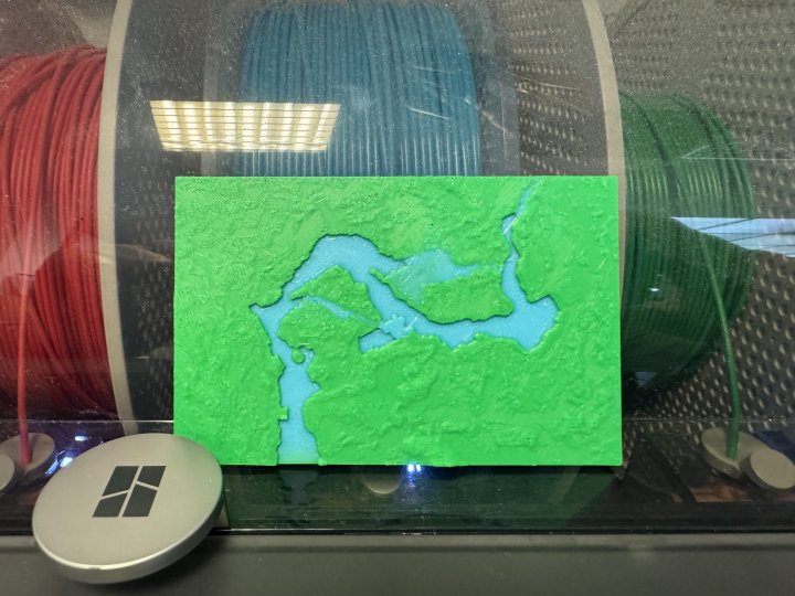 A photo of a small plastic 3D-print showing a blue river running through a green landscape.