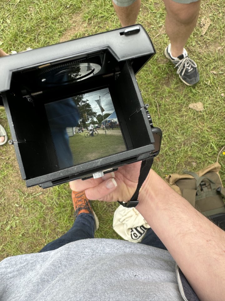 A photo looking down the view finder of an old TLR camera. The view shows an out of focus torso and a circus tent in the background.