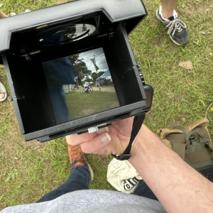 A photo looking down the view finder of an old TLR camera. The view shows an out of focus torso and a circus tent in the background.