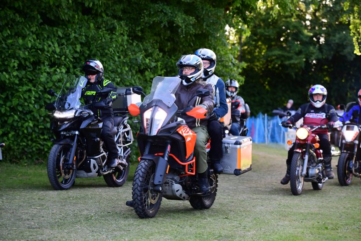 A photo of two people on a motorcycle driving along a grass lane next to a wall of trees, with a few other motorcycles near by. The main bike is a big KTM adventure bike, on which is my and Laura.