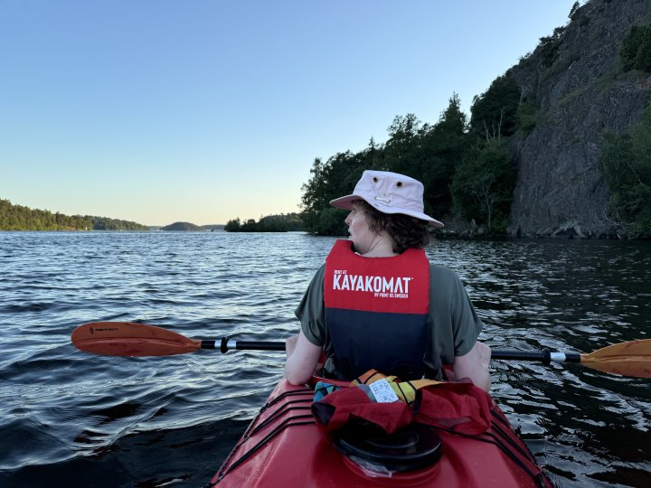 A photo from the back of the kayak again, looking forward to Laura in the front and beyond along the lake. This time though there is a rock cliff to our right rather than the forest trees in other shots.