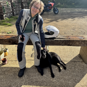 A photo of Laura sat on a bench in her motorcycle outfit, and lent against her leg is a black labrador dog, as if it's known her its entire life (they met about two minutes earlier). In the background sits the bright orange of a large KTM adventure motorbike.