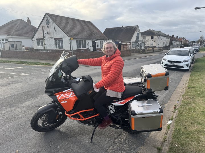 A photo of a woman in an orange winter coat sat on a large orange and black adventure bike.