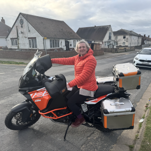 A photo of a woman in an orange winter coat sat on a large orange and black adventure bike.