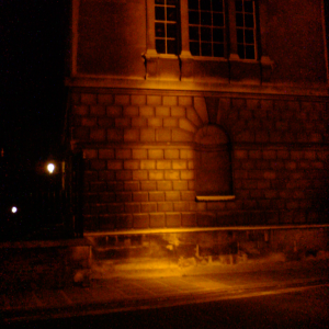 A picture of an old stone cambridge building in the dark, which a line of sodium coloured light running up the middle.