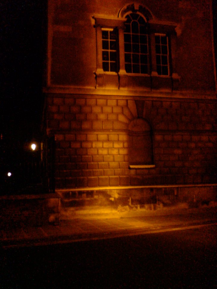 A picture of an old stone cambridge building in the dark, which a line of sodium coloured light running up the middle.