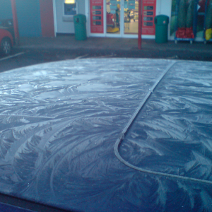 The top of a car is covered with a pretty layer of frost in a very crystaline pattern.