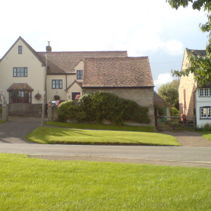 A picture of a fancyish house in an england village with a hedge growing up the wall. The outline of the hedge looks somewhat like a giant pig.