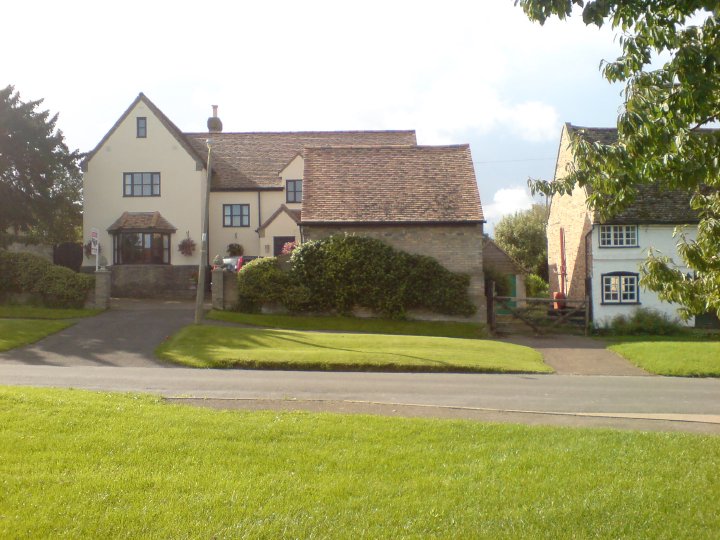 A picture of a fancyish house in an england village with a hedge growing up the wall. The outline of the hedge looks somewhat like a giant pig.