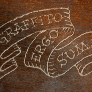The words 'Graffito Ergo Sum' etched into some wood as if on a scroll.