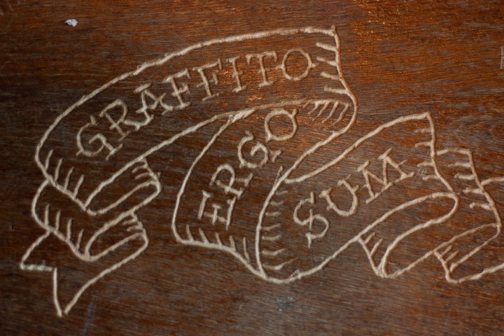 The words 'Graffito Ergo Sum' etched into some wood as if on a scroll.