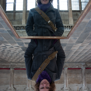 A photo of Laura looking into a mirror laid on a table in Ely Cathedral, to make it easier to see the ceiling. The photo is looking at Laura in the mirror, and the whole picture has been flipped to mirror Laura is the right way up, and non-mirror Laura is where the relfection should be.