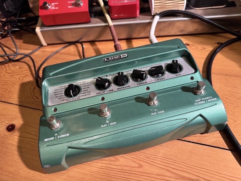 A photo of a large guitar effects pedal, which is green, and has four stomp buttons on it and 6 rotary dials. It is a Line 6 DL4 delay modeller.