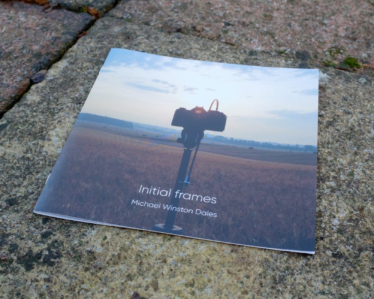 A photo of the cover of the zine, showing the view from behind a film SLR camera on a tripod, as the camera looks out over some fields.